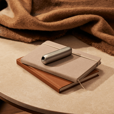 Ploom AURA front panels with Jet Black Augmented Pattern placed on top of a stack of notebooks.
