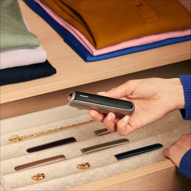 Hand holding Ploom AURA front panel Jet Black Augmented Pattern accessory on device.

