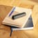 Ploom device with Jet Black Back Cover on top of a stack of notebooks
