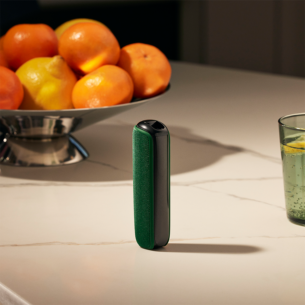 Ploom device with Amazon Green Back Cover on a table close to a fruit basket
